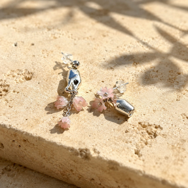 Pink Lily of the Valley drop earrings on a sunlit limestone surface, photographed on a textured beige stone surface with natural sunlight and leaf shadows.