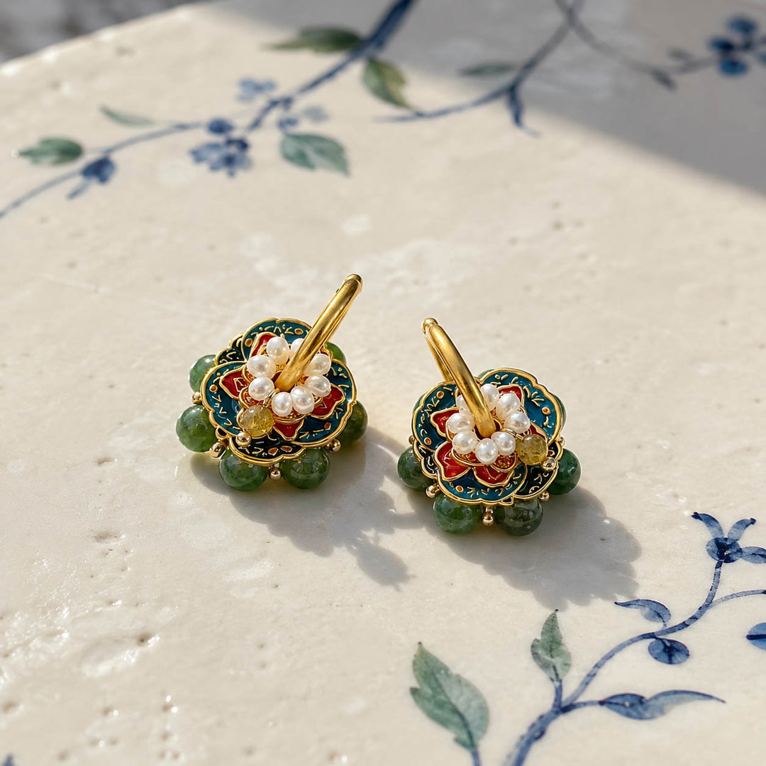 Moss Garden convertible hoop earrings with hand-painted enamel, pearls and green gemstones displayed on a cream-colored ceramic surface with blue floral painted motifs.