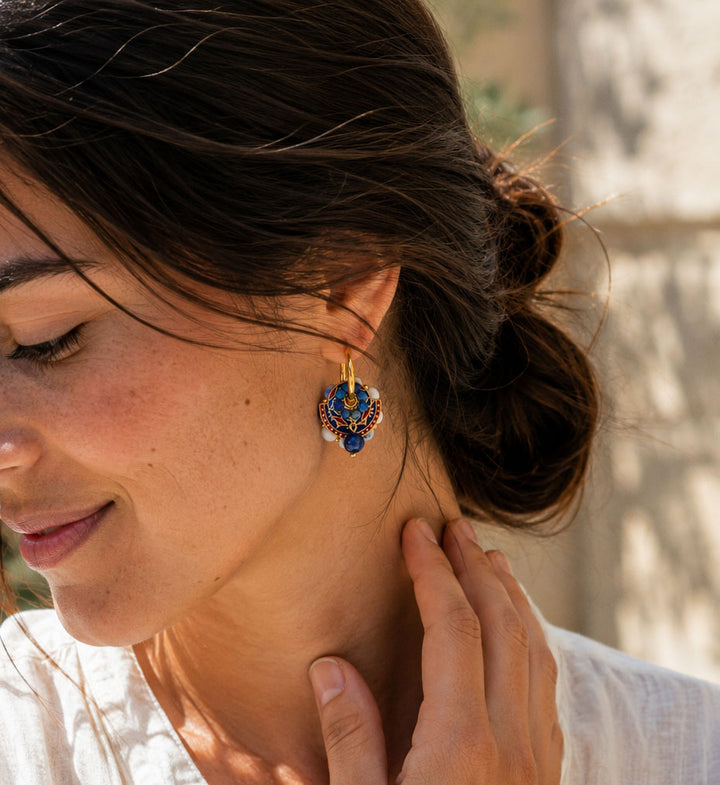 A close-up lifestyle shot of a woman wearing a convertible gold hoop earrings with blue-and-white porcelain beads. set against a softly blurred outdoor background.
