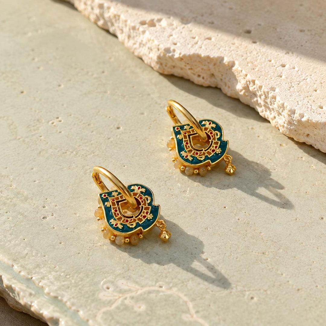 Teal hand-painted enamel convertible hoop earrings with Yellow Jade bead accents, resting on a textured beige stone surface.