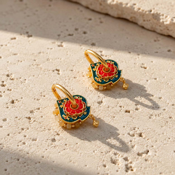 A pair of gold hoop earrings with red and teal hand-painted enamel convertible hoop earrings with Yellow Jade beads, resting on a textured beige stone surface in bright sunlight.