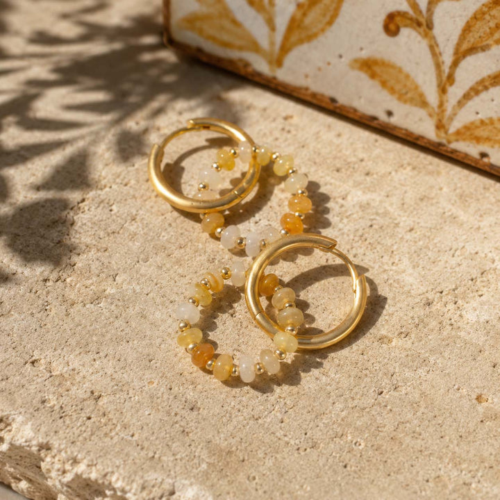 Yellow Jade beaded gold hoop earrings with removable gemstone rings, arranged on a textured beige stone surface in warm sunlight.