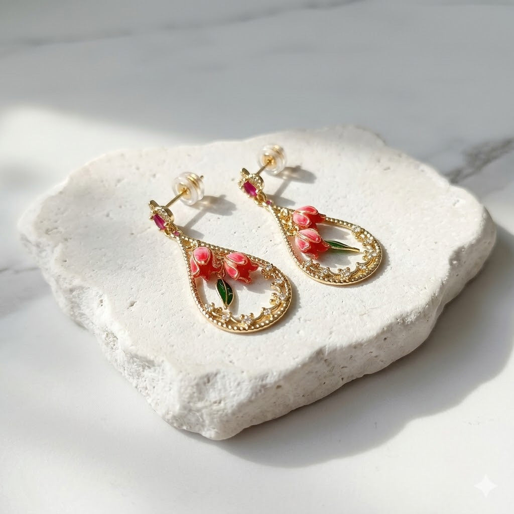 Gold earrings with floral designs on a white stone surface