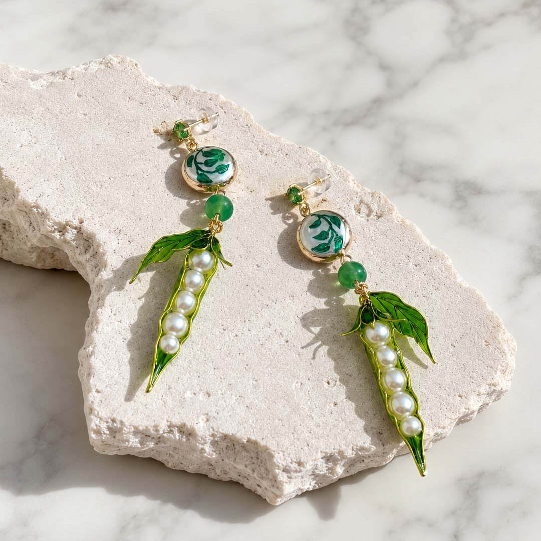 Pea Pod &amp; Baroque Pearl Drop Earrings featuring hand-painted enamel pea pods, glass pearls, hand-painted baroque pearls, jade beads and CZ studs on a textured white stone surface.