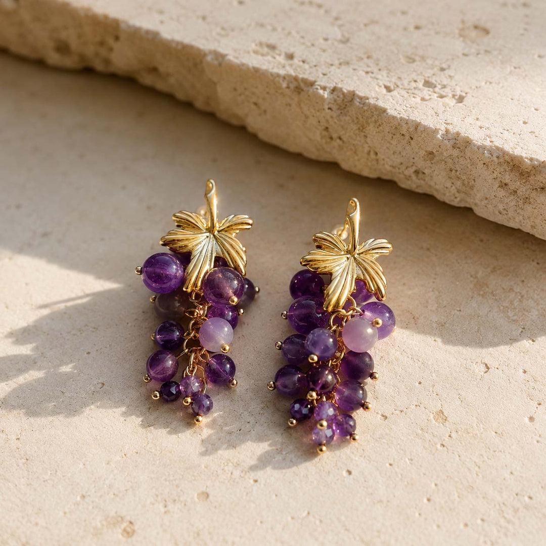 Natural amethyst grape cluster earrings with 18K gold-plated brass resting on a textured limestone surface.