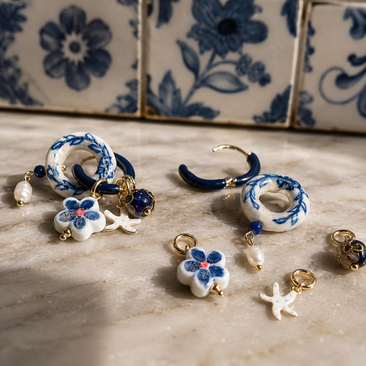 Interchangeable components of A2K convertible hoop earrings with blue and white porcelain, cloisonne, and lapis beads, displayed on a beige marble surface in front of blue and white patterned tiles.