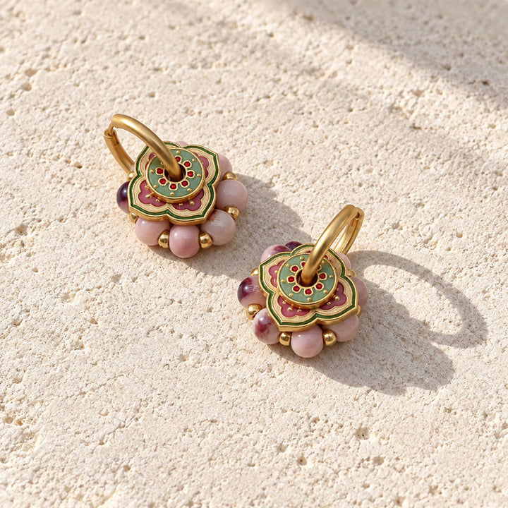 Pink hand-painted porcelain bead convertible hoop earrings with 18K gold-plated hoops, placed on cream color stone surface.