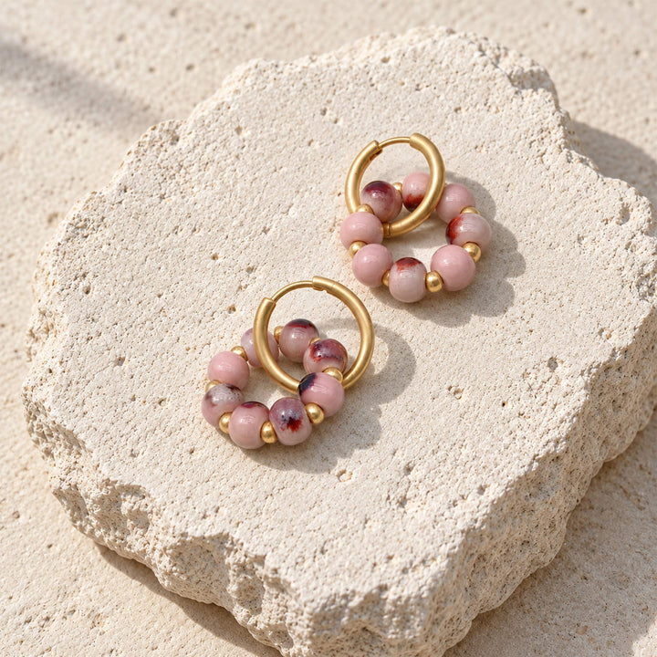 Convertible hoop earrings with pink porcelain beads , placed on cream color stone surface.