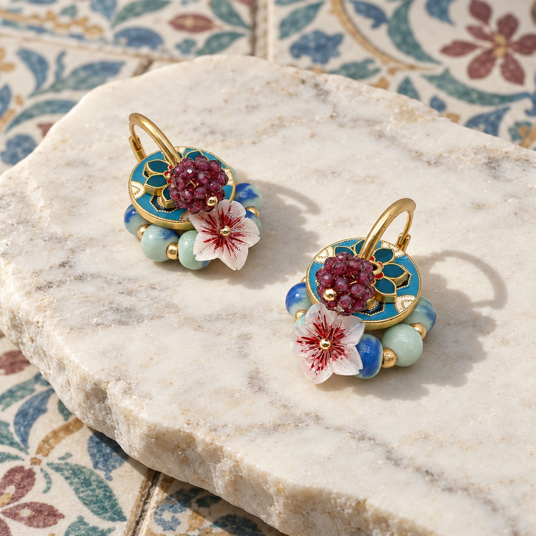 Garnet and sakura convertible earrings with layered enamel and porcelain beads on a marble surface with floral tiles.