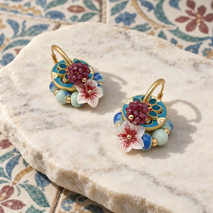 Garnet and sakura convertible earrings with layered enamel and porcelain beads on a marble surface with floral tiles.
