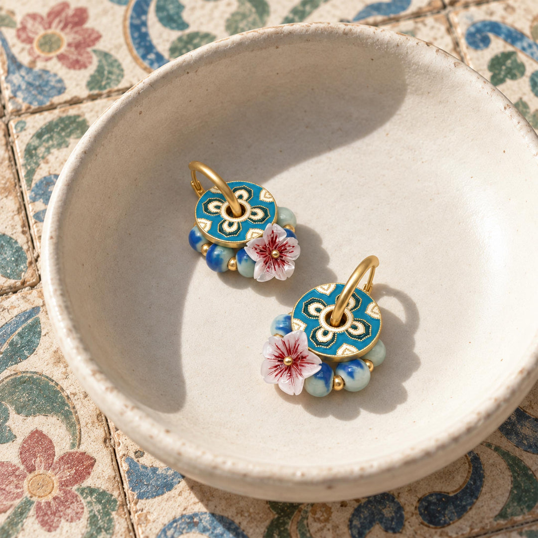 Garnet and sakura convertible hoop earrings with hand-painted porcelain beads, displayed in a ceramic bowl on patterned tiles.