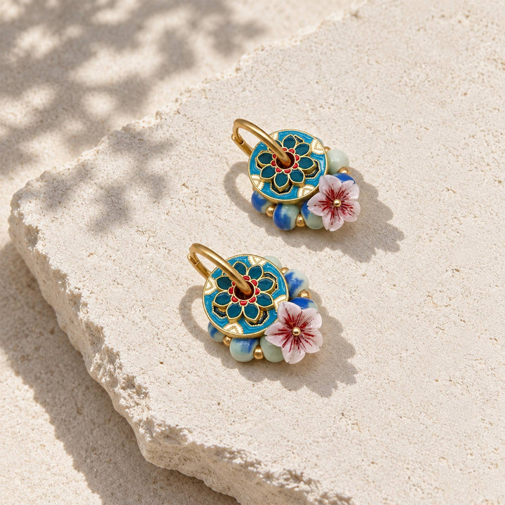 Convertible garnet hoop earrings with blue-green porcelain beads and mother-of-pearl sakura flowers on a sunlit stone slab.