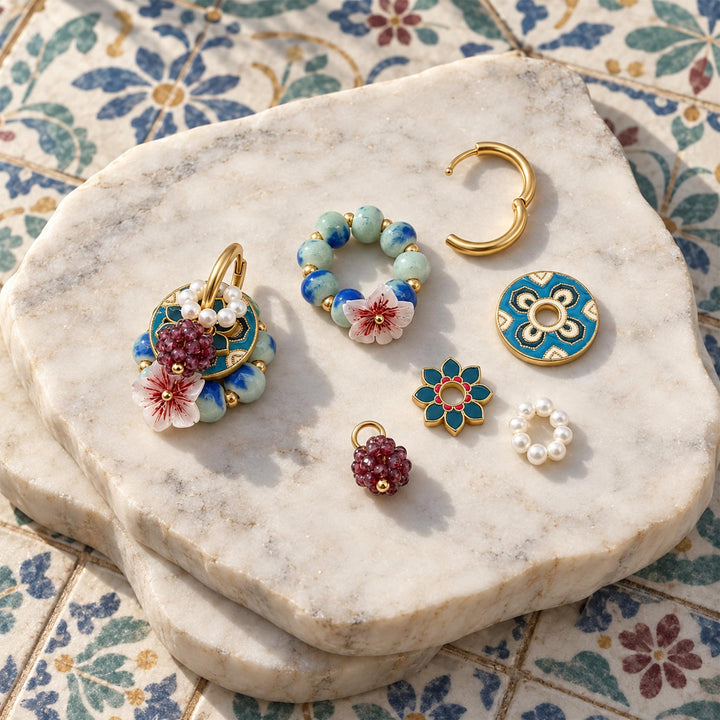 Convertible earrings with garnet, freshwater pearls, hand-painted enamel and mother-of-pearl flower components arranged on a marble slab.