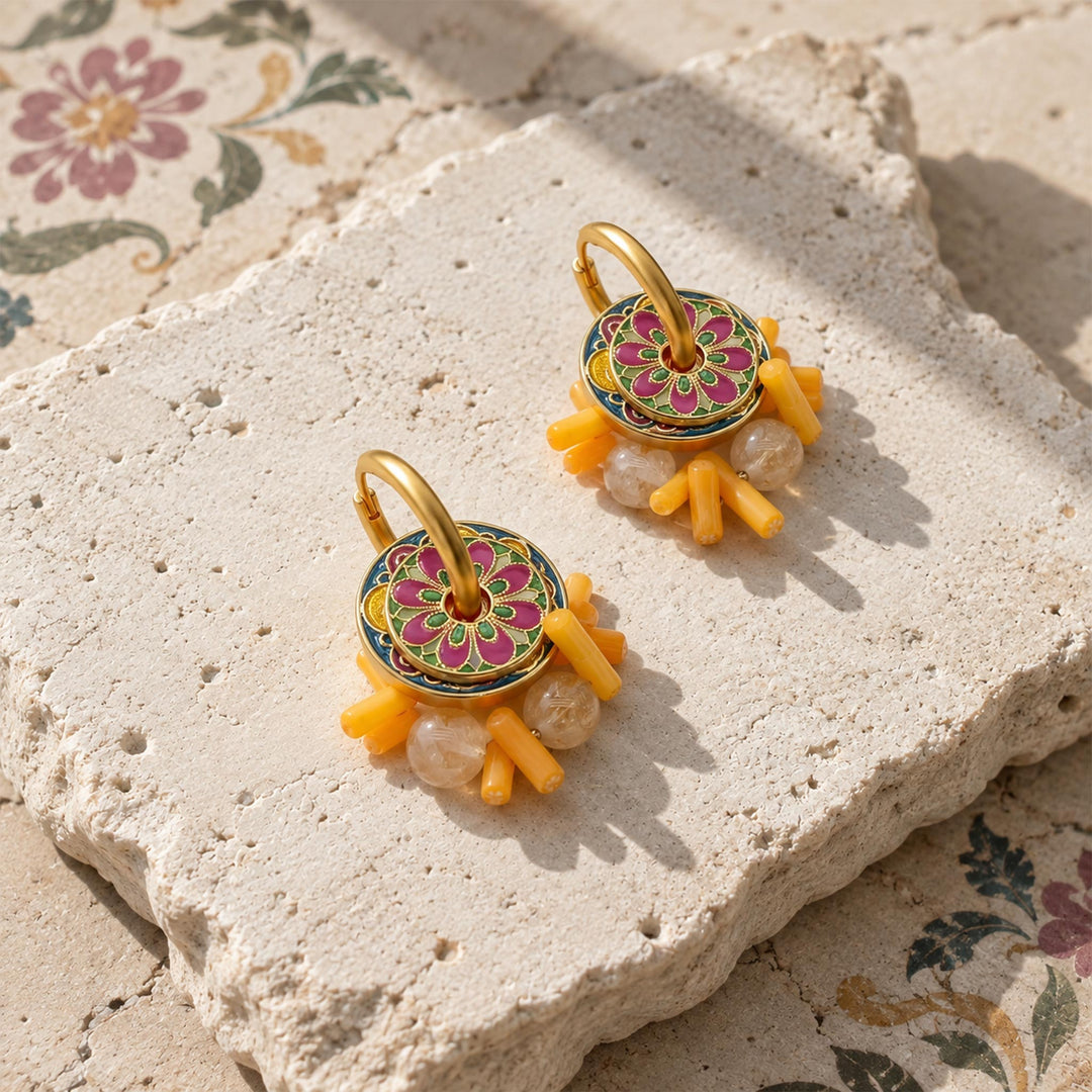 Citrine and coral convertible hoop earrings with hand-painted enamel, displayed on a textured stone slab.