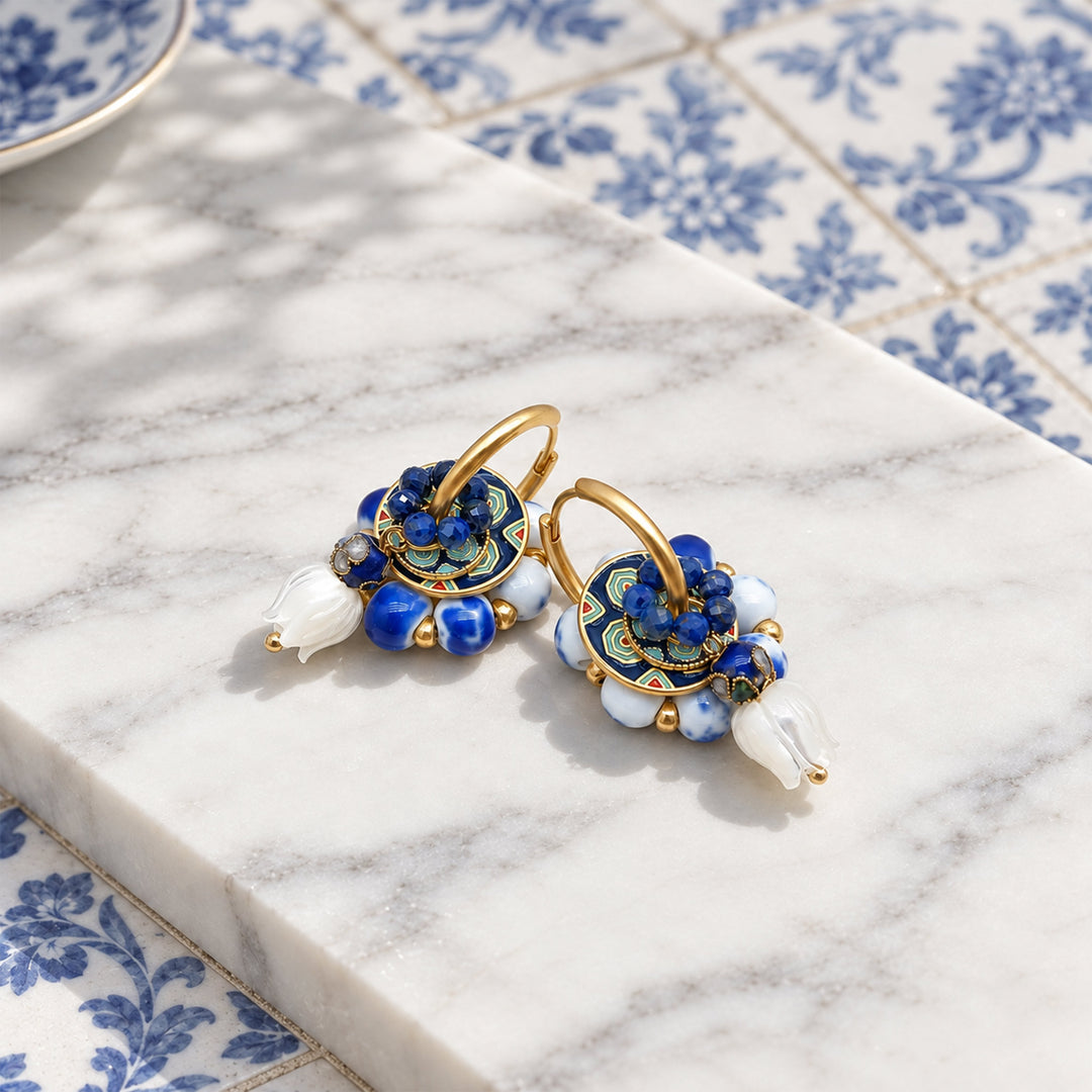 Convertible lapis hoop earrings with removable porcelain, enamel and mother-of-pearl components, displayed on a white marble slab over blue patterned tiles.