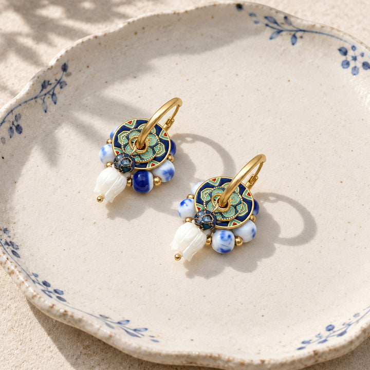 Lapis tulip convertible hoop earrings with porcelain beads and mother-of-pearl tulip drops, displayed on a beige ceramic plate with blue floral pattern