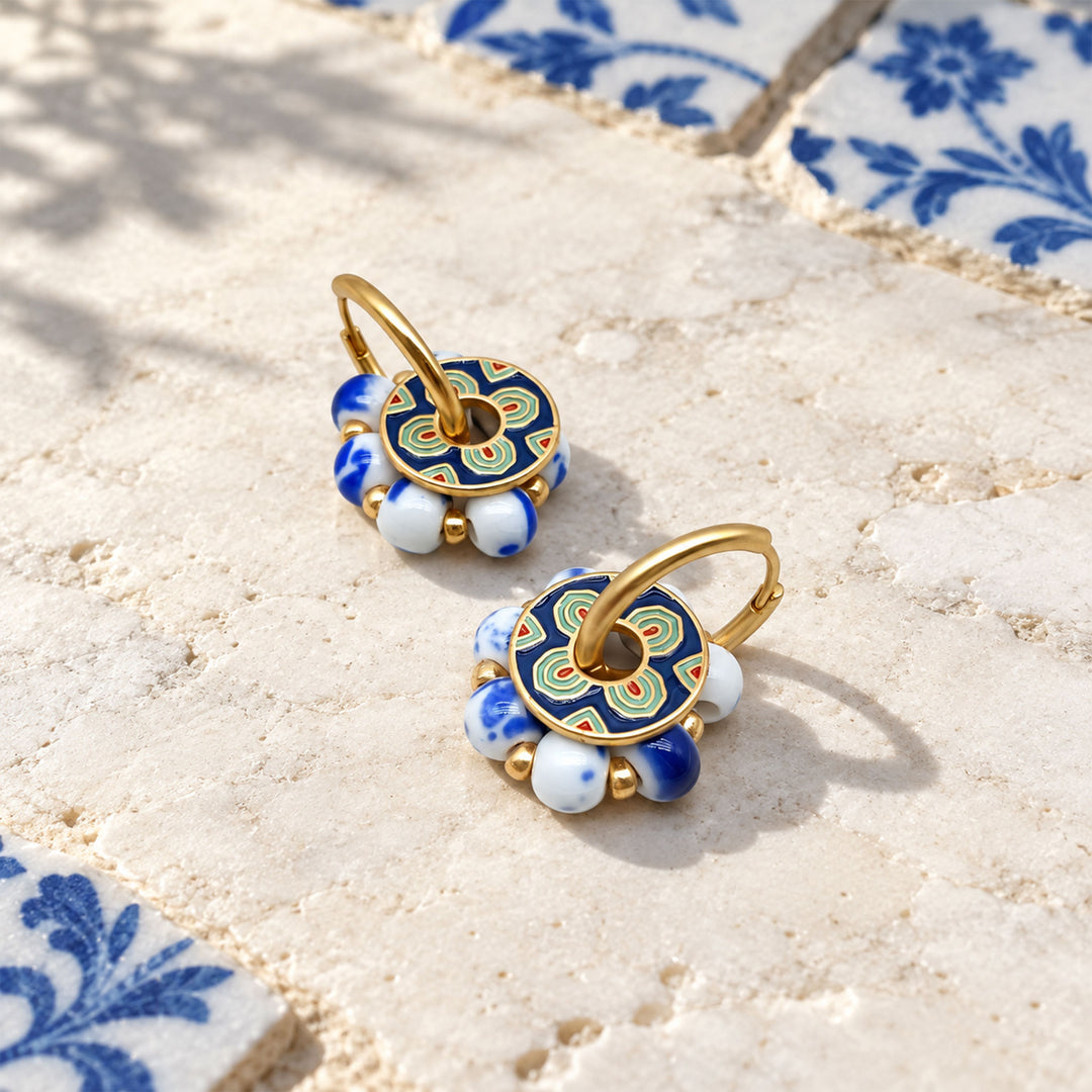 Lapis and porcelain convertible hoop earrings with enamel details on a sunlit pale stone surface, displayed on a textured beige stone surface with blue patterned tiles in the background.