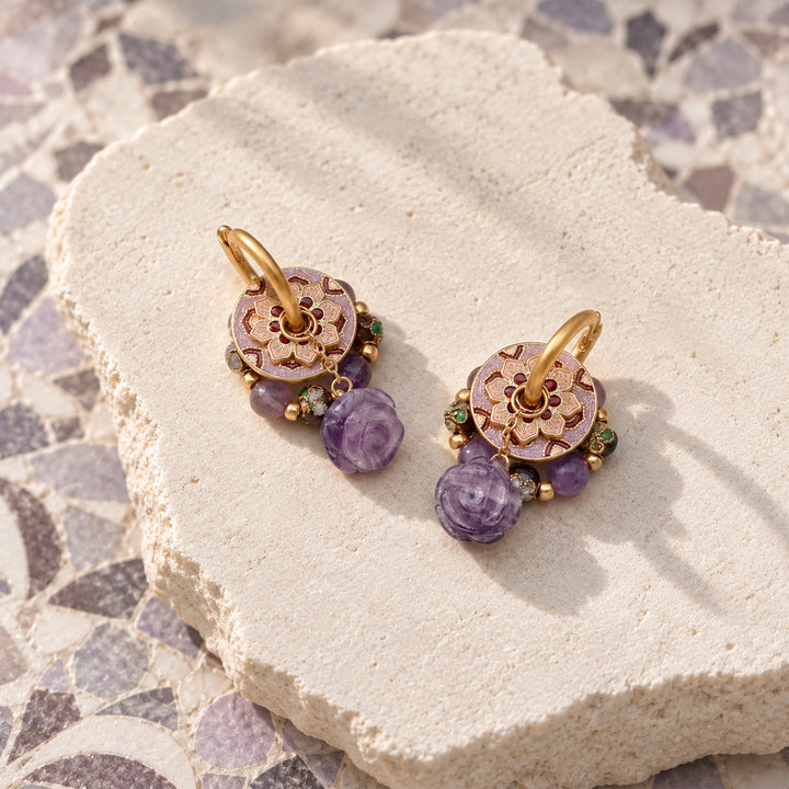 Amethyst rose convertible earrings with enamel and cloisonné details, displayed on a textured beige stone slab over a mosaic tile surface.