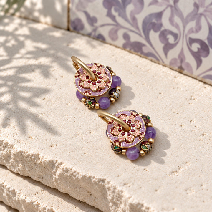 Amethyst convertible hoop earrings with enamel floral discs and cloisonné beads on a sunlit pale stone surface.