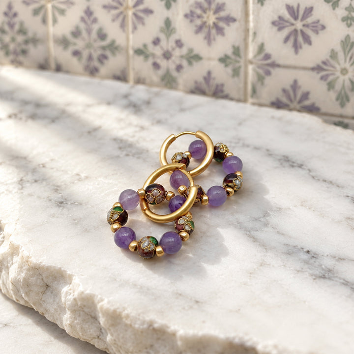 Amethyst and cloisonné bead convertible hoop earrings on white marble with lavender floral tiles.