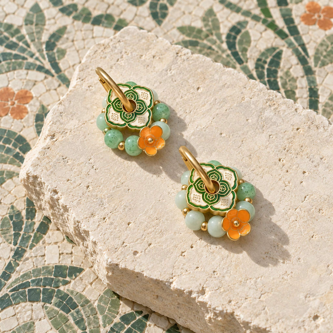Convertible hoop earrings with green agate, porcelain beads and orange enamel flowers on a pale stone slab.
