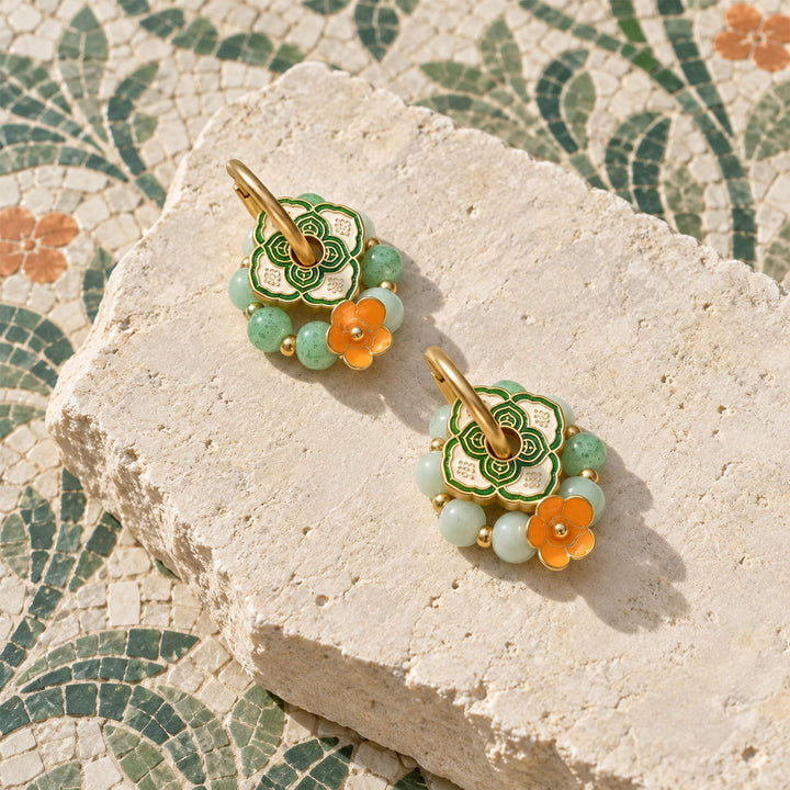 Convertible hoop earrings with green agate, porcelain beads and orange enamel flowers on a pale stone slab.