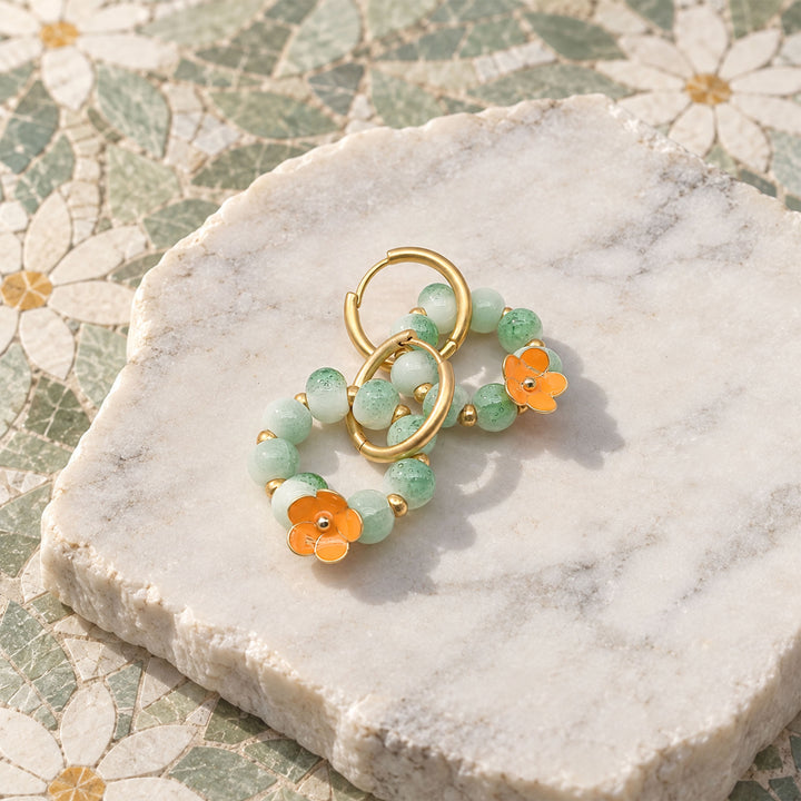 Green agate and enamel flower convertible hoop earrings displayed on a marble slab with floral mosaic background.