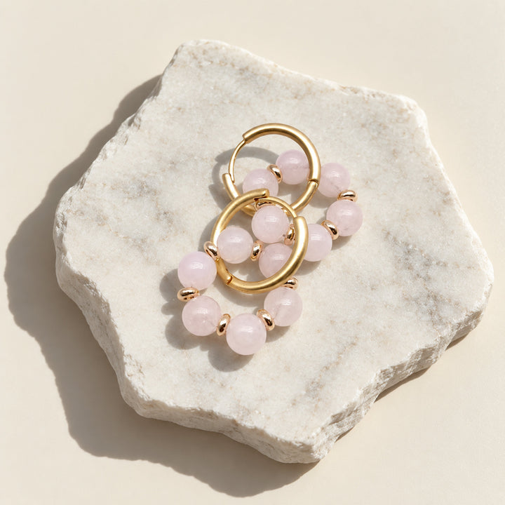 Simple pink quartz convertible hoop earrings arranged on a pale stone slab in direct sunlight.