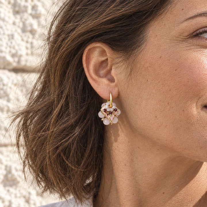 Model wearing pink quartz and garnet convertible hoop earrings outdoors against a pale stone wall.