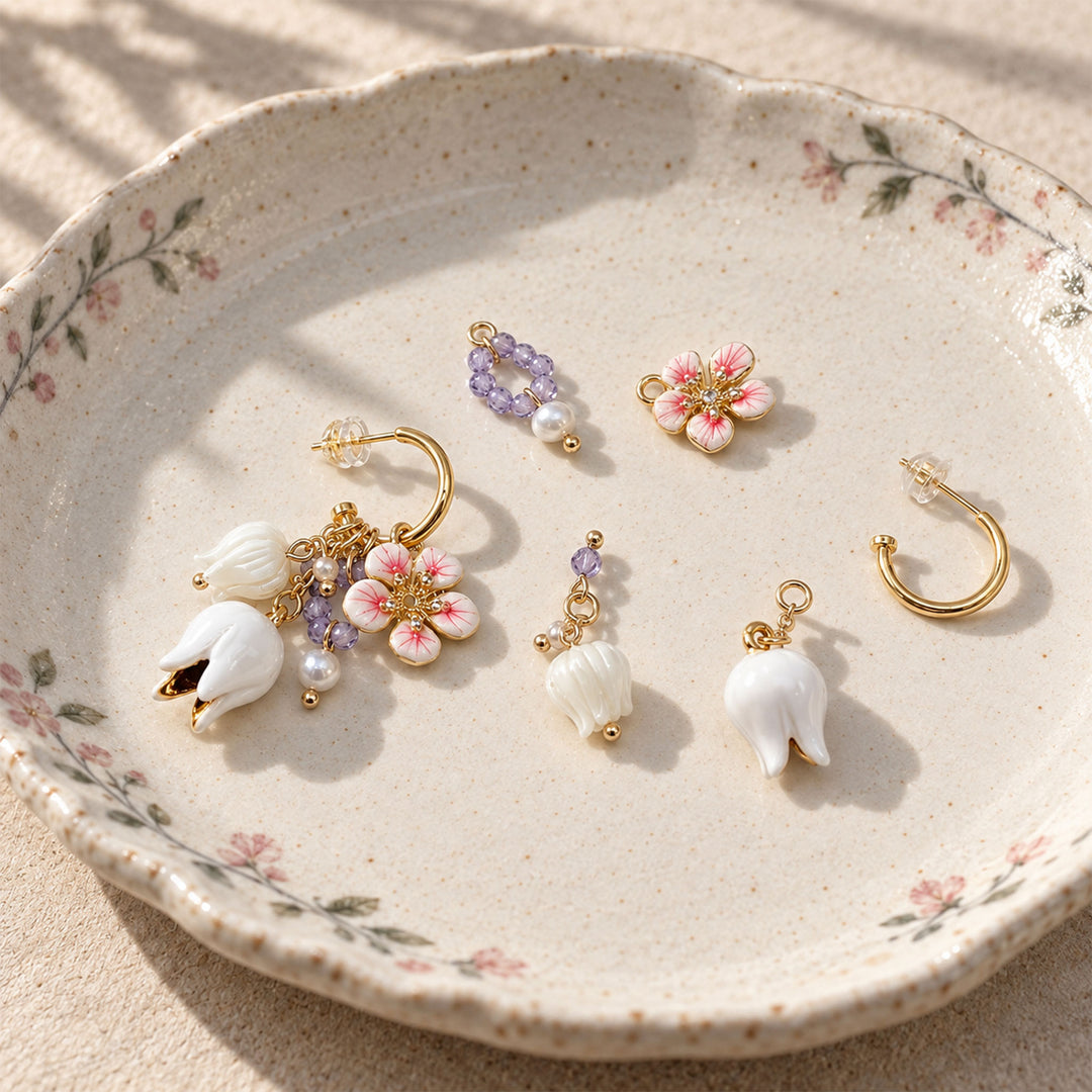 Convertible earrings with mother-of-pearl Lily of the Valley flowers, amethyst beads and enamel charms arranged in a floral ceramic dish.