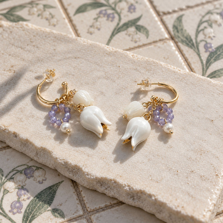Lily of the Valley convertible earrings with mother-of-pearl flower drops, amethyst and freshwater pearls on a sunlit stone slab.
