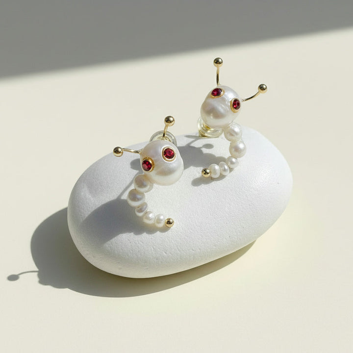 Pair of pearl earrings with red gemstones on a white stone