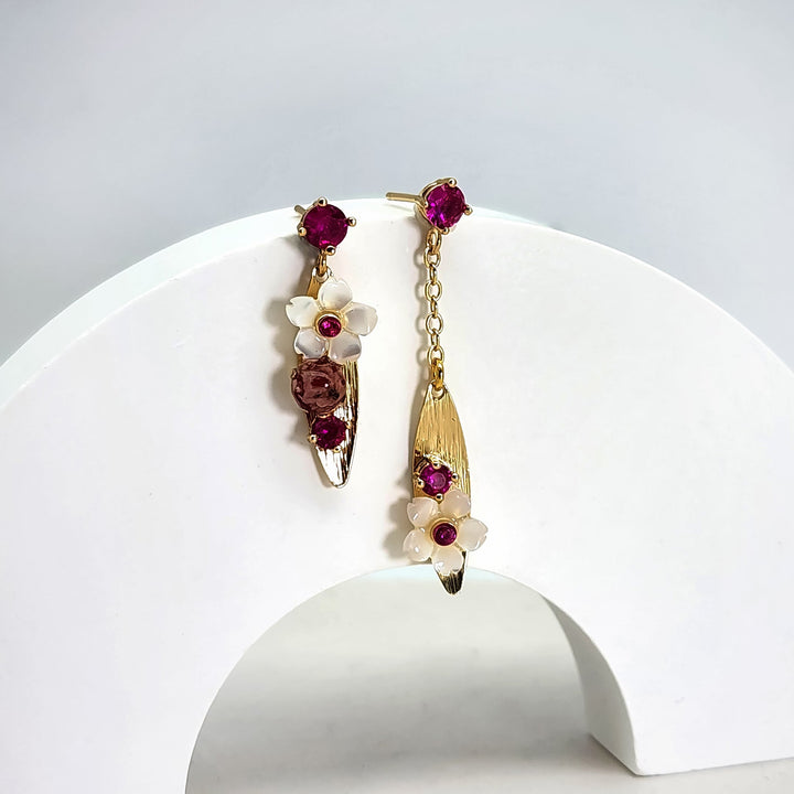 Pair of floral earrings with red gemstones on a white stand