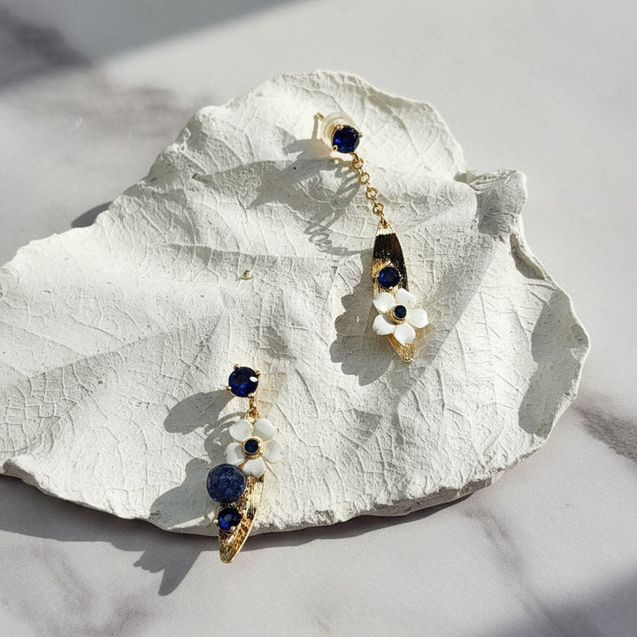 Gold earrings with blue gemstones on a white leaf