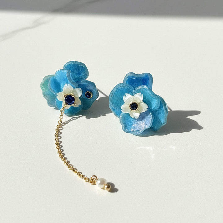 Blue floral earrings with a gold chain on a white background