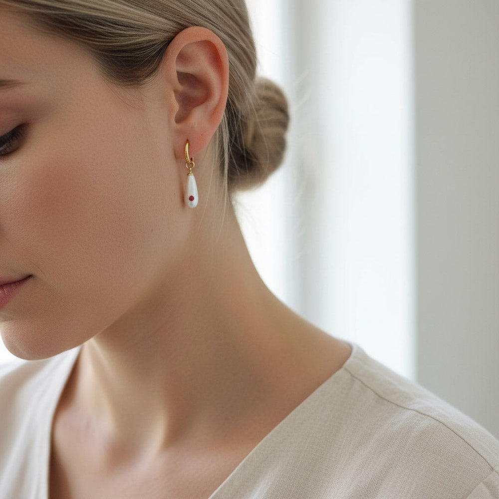 Close-up of a woman wearing a gold earring with a pearl-like bead.