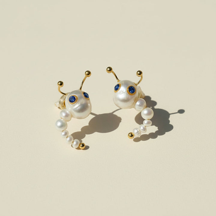 Pair of pearl earrings with gold accents on a beige background