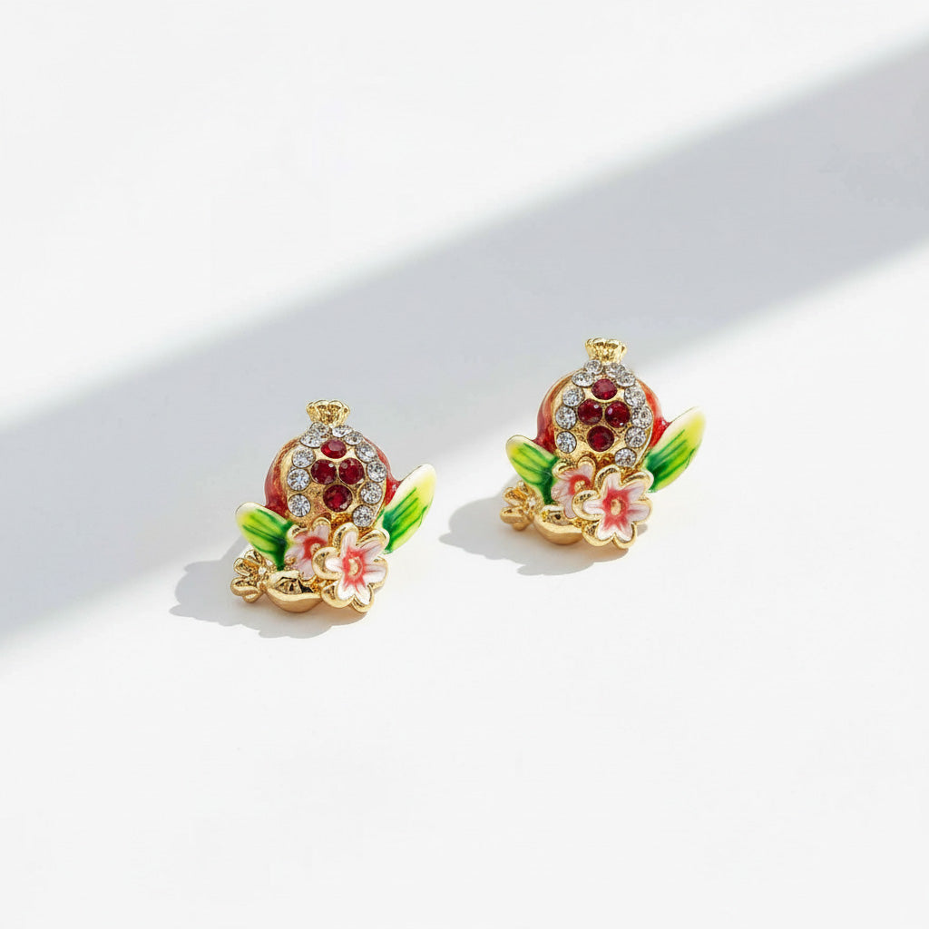 Artistic pomegranate enamel earrings under sunlight.