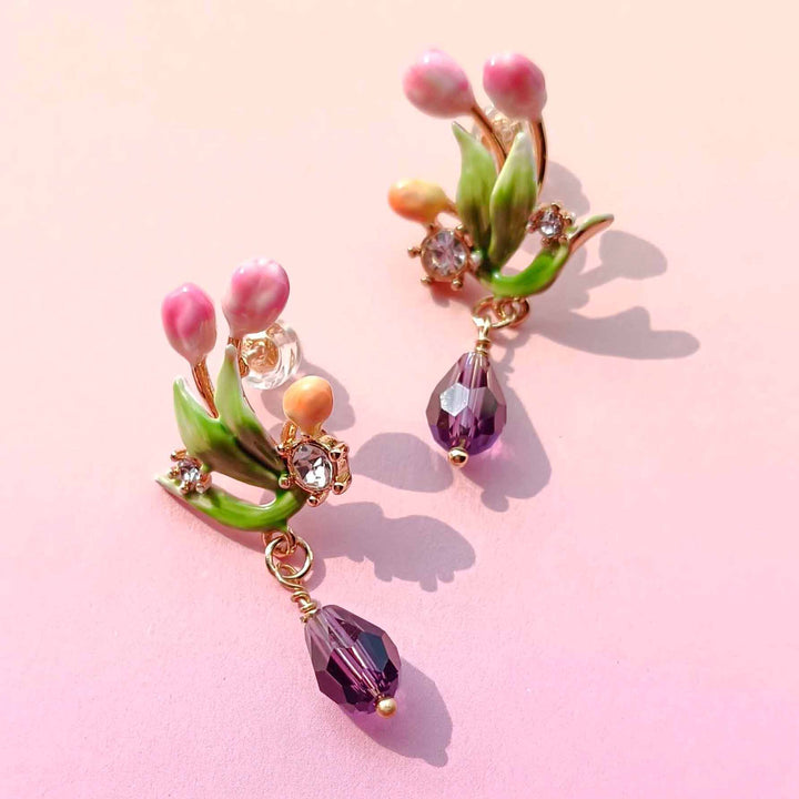 Pair of floral earrings with pink flowers and purple beads on a pink background