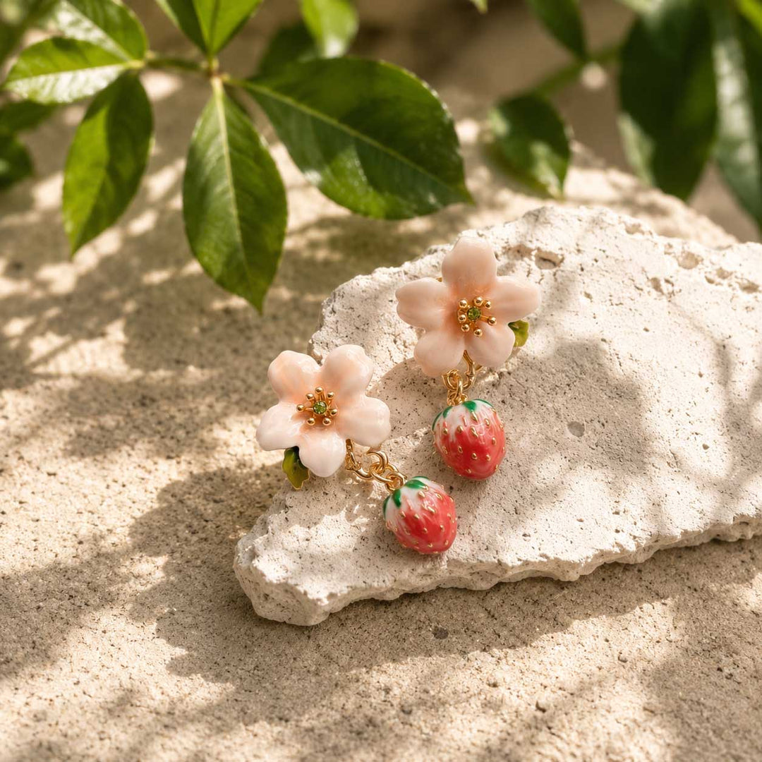 Aesthetic flat lay of pink blossom flower earrings with dangling strawberry charms on a rustic desert stone under warm natural sunlight, nature-inspired jewelry display.