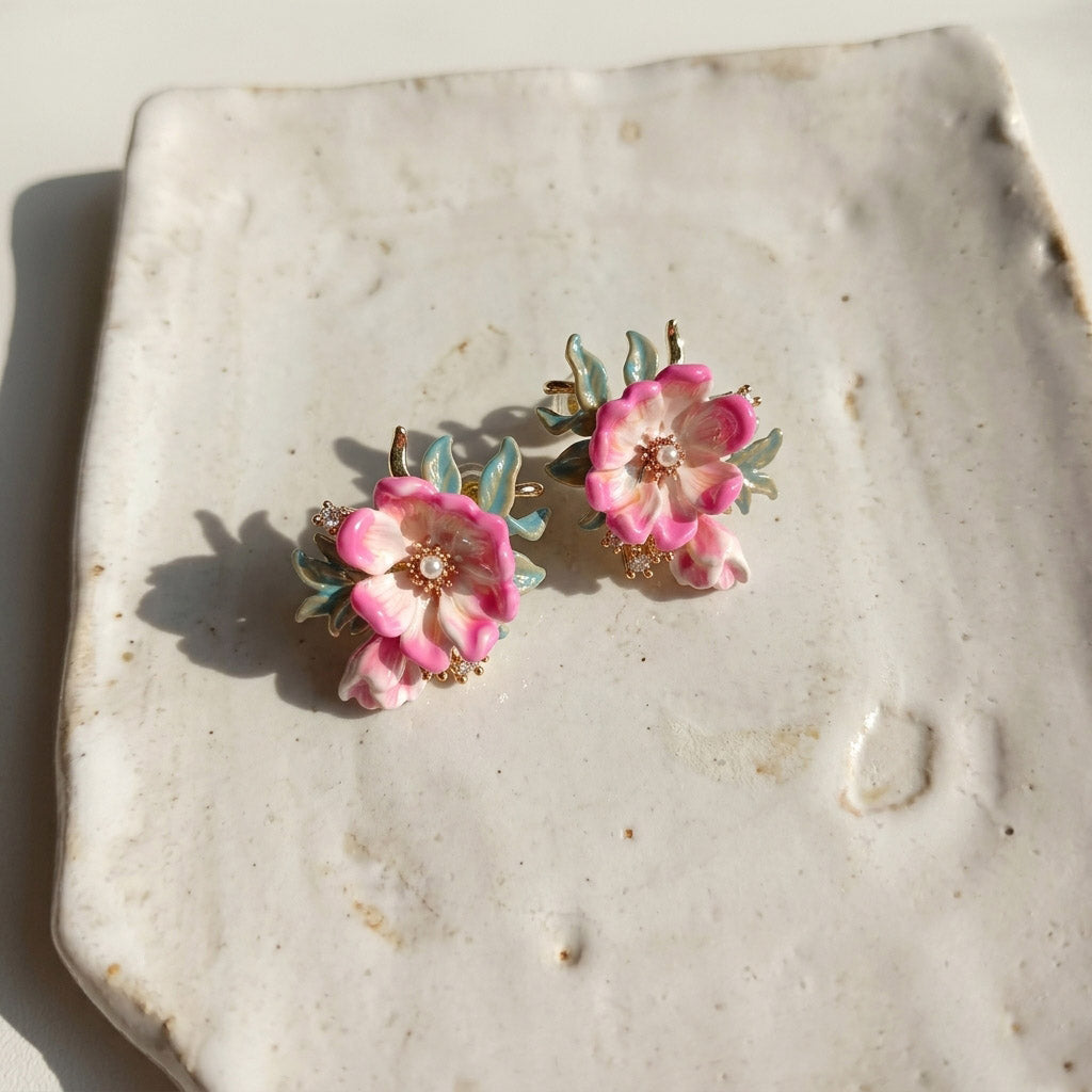 Pair of pink floral earrings on a textured stone surface