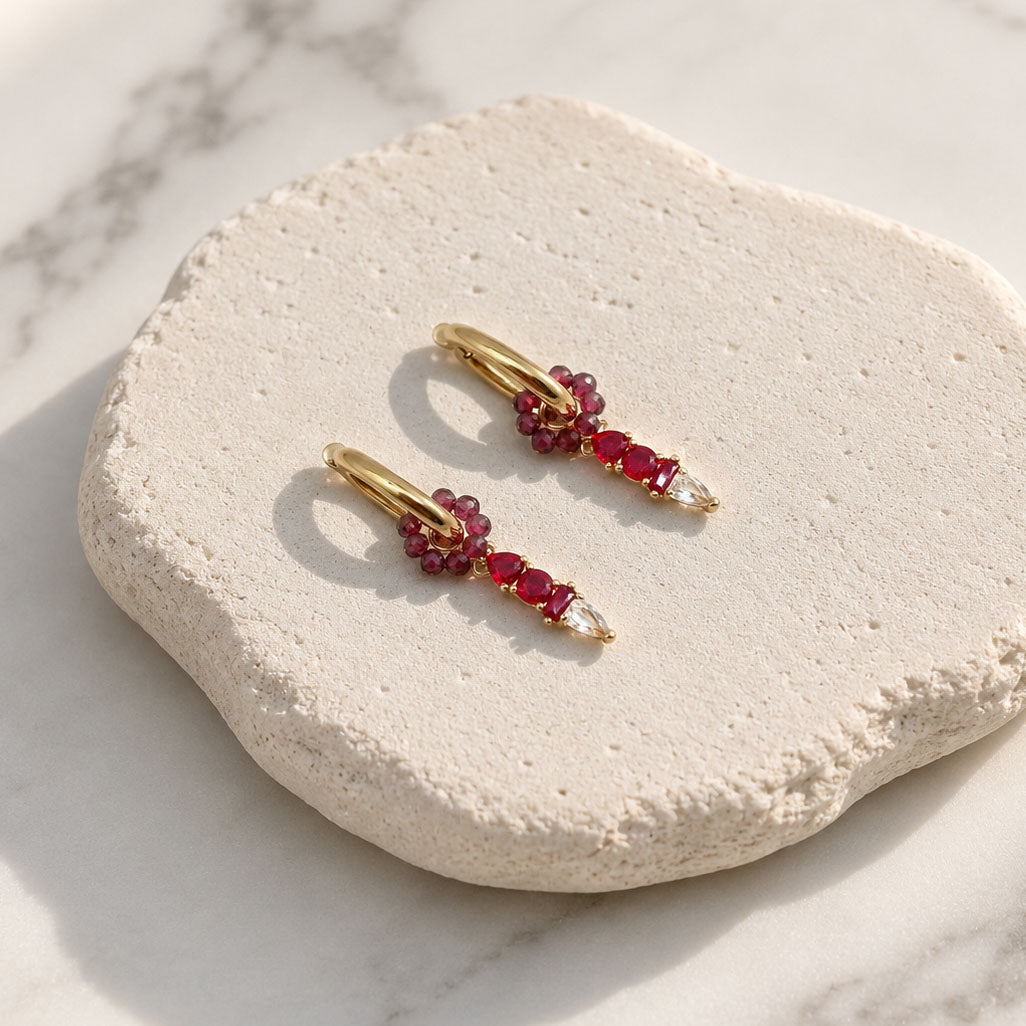 January Garnet huggie earrings with removable garnet semi-precious stone floral ring and CZ glass birthstone charm displayed on a textured white stone surface.