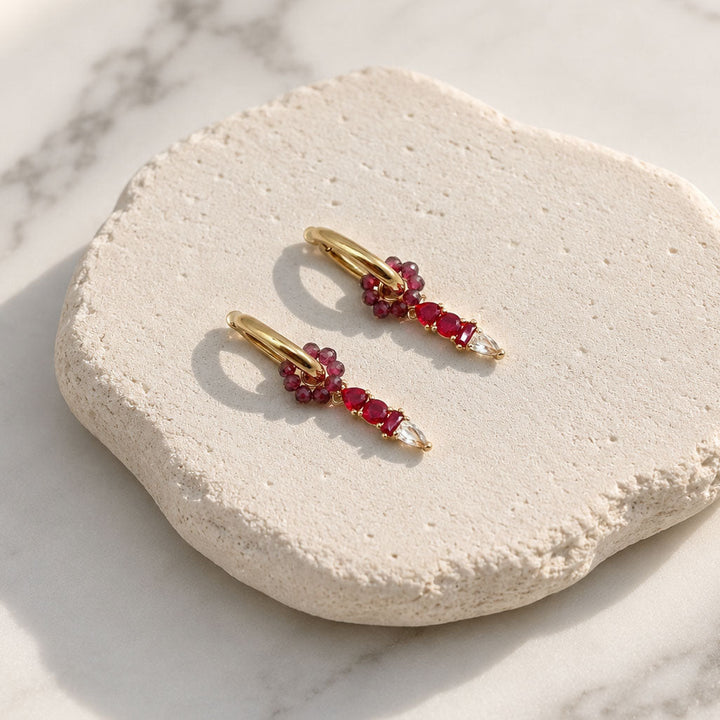 January Garnet huggie earrings with removable garnet semi-precious stone floral ring and CZ glass birthstone charm displayed on a textured white stone surface.