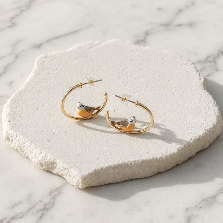 Gold hoop earrings with bird designs on a textured stone surface.