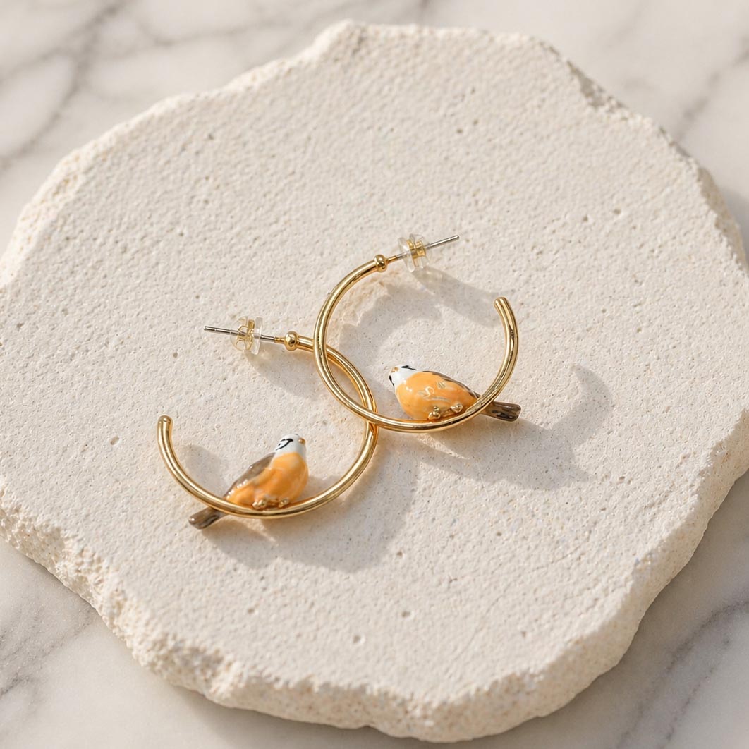 Gold hoop earrings with bird designs on a textured white surface