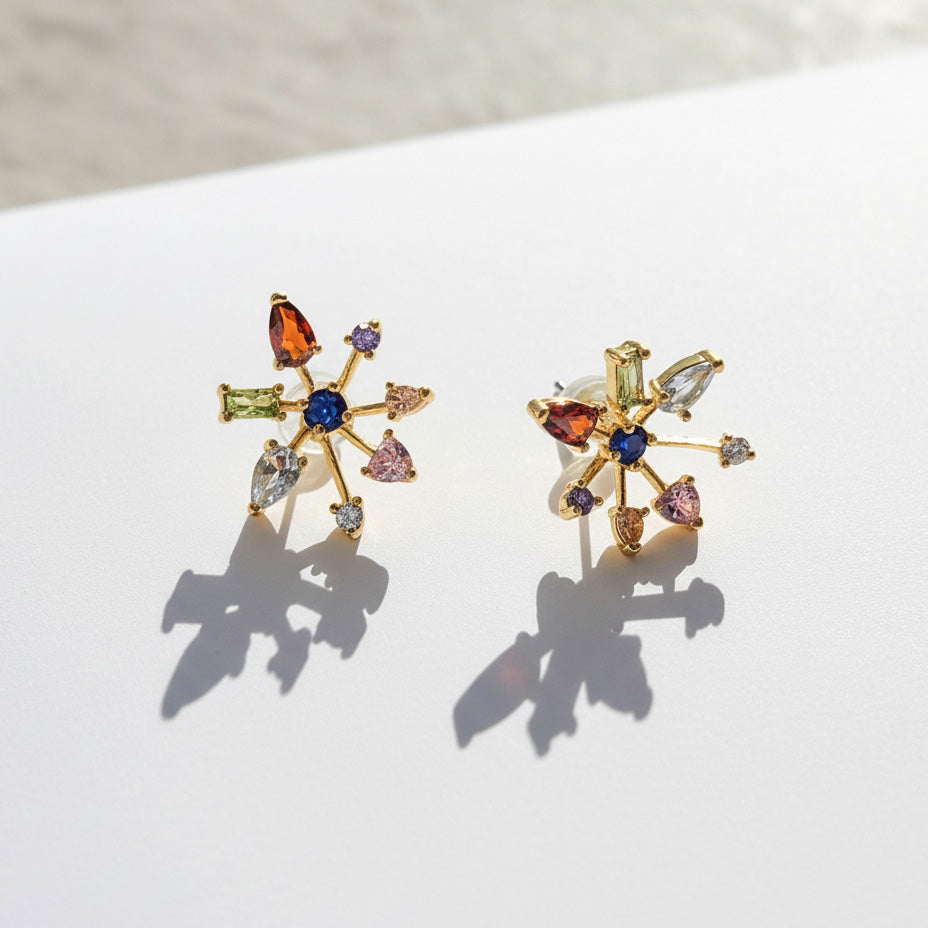 Gold plated multicolor CZ starburst stud earrings photographed in sunlight on white surface.