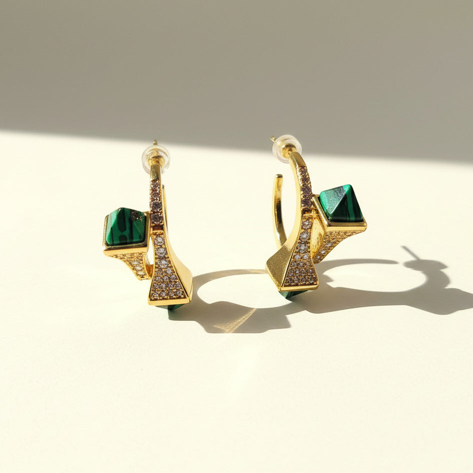 Gold earrings with green gemstones on a beige background