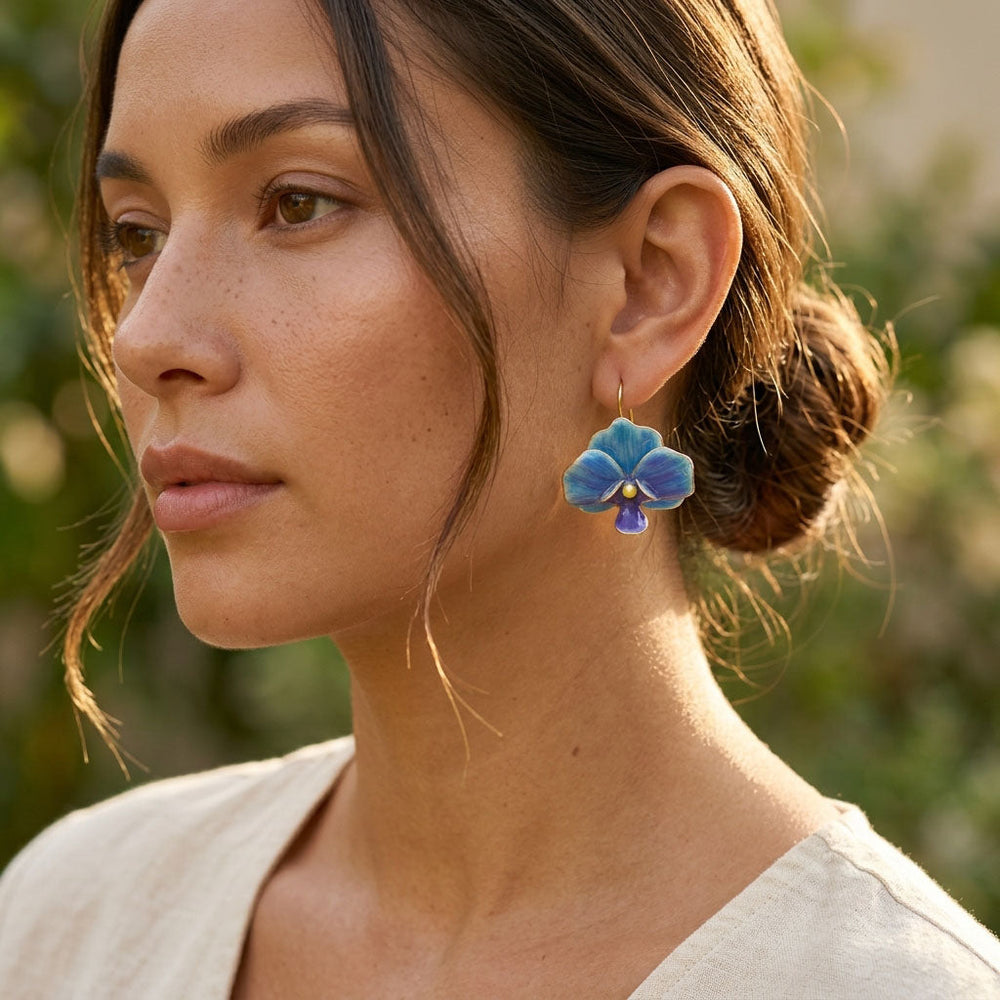 Woman wearing blue orchid earrings with a blurred natural background