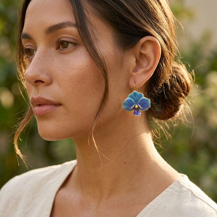 Woman wearing blue orchid earrings with a blurred natural background