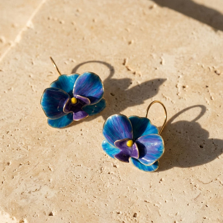 Blue flower-shaped earrings on a beige stone surface